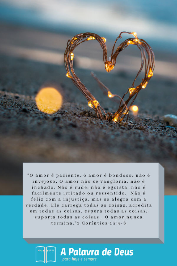 Um coração entrelaçado com pequenas luzes se projeta da areia. As palavras de 1 Coríntios 13:4-8 são escrita