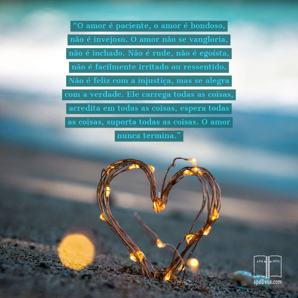 Um coração entrelaçado com pequenas luzes se projeta da areia. As palavras de 1 Coríntios 13:4-8 são escrita