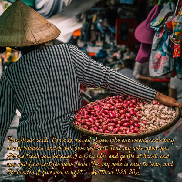 Você não acha reconfortante poder confiar em um Deus que se importa com seu cansaço e não o considera um fardo? Uma mulher com um chapéu de palha carrega uma grande bandeja com frutas por um mercado ao ar livre.